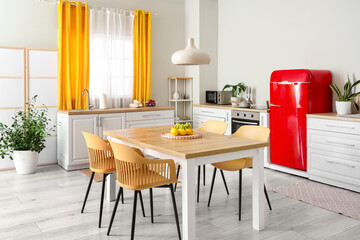 Interior of modern kitchen with white counters, dining table, red fridge, chairs and lamp