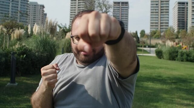 Man in glasses with extra weight boxing in public park to give fight to sugar and overeating