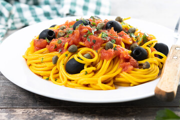 Italian Pasta puttanesca with tomato sauce, capers, and black olives on wooden table