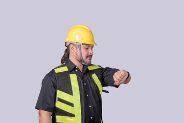 Studio shot of a barrel-chested construction worker in safety gear looking at his wristwatch, symbolizing time management on site.