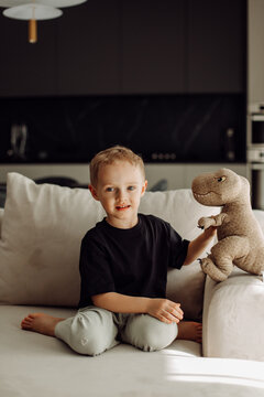 Smiling child playing with plush dinosaur toy on sofa in living room