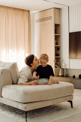 Mother kissing her toddler son while playing on sofa in modern living room