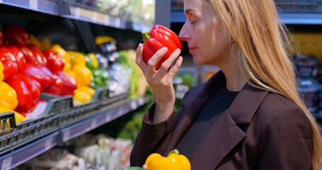 Woman choosing and smells red bell pepper while selecting vegetables