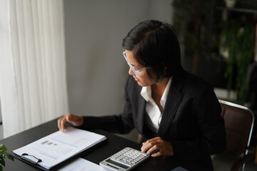 Asian businesswoman sits on chair using calculator calculate company finance documents