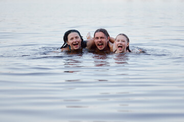 A joyful family moment of three people swimming happily in a serene, peaceful lake.