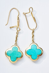 Elegant Gold Dangling Earrings with Turquoise Four-Leaf Designs on White Background..