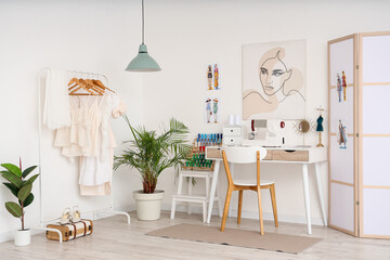 Interior of light atelier with tailor's workplace, clothes rack and folding screen