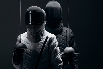 Two Fencers in Protective Gear Posing with Swords Against a Dim Background..