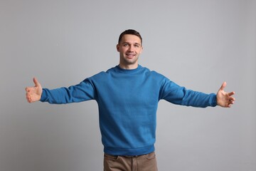 Cheerful man welcoming guests on light grey background