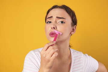 Beautiful woman shaving her mustache with razor on light green background