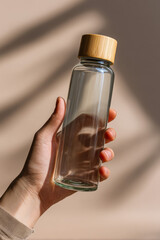 close-up of a hand holding a reusable glass bottle with bamboo lid
