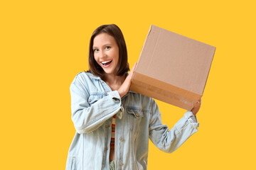 Beautiful young happy woman with parcel box on yellow background