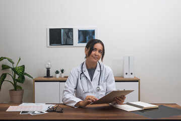 young female therapist doctor looking at camera meticulously reviews patient test results while...