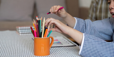 Colorful Creativity. A teenage girl with Down syndrome selects colored pencils from a cup during an...