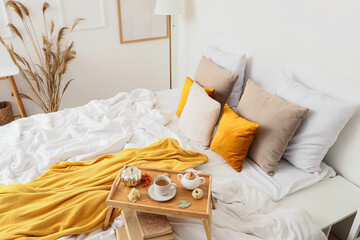 Plaid and tray with tea on bed in cozy bedroom