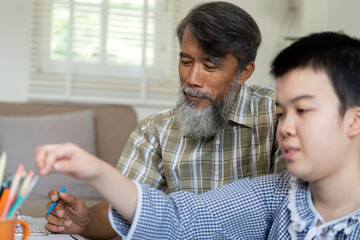 Art and Connection. A teenage girl with Down syndrome focuses on her drawing while her grandfather...