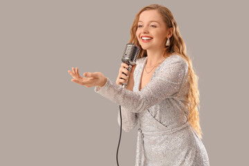 Beautiful woman with microphone singing karaoke on light background
