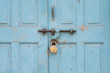 Old weathered door locked with a padlock, blue shabby color, India
