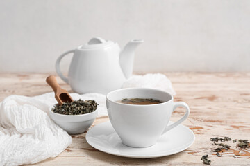 Cup and teapot of hot green tea with dried leaves on white wooden table