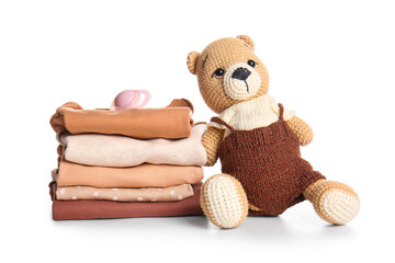 Stack of baby clothes, pacifier and teddy bear on white background