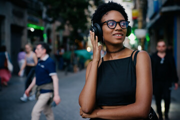 Chic young woman laughs joyfully in city street while enjoying her favorite tunes, embracing digital freedom, style, and positive emotion through wireless headphones