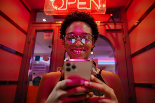 Fashionable woman immersed in smartphone screen, sitting under red neon glow, actively engaging with mobile content or social platforms