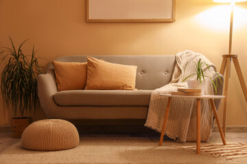 Interior of stylish living room with grey sofa, coffee table and glowing standard lamp at evening