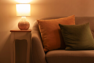 Interior of stylish living room with grey sofa, coffee table and glowing lamp at evening