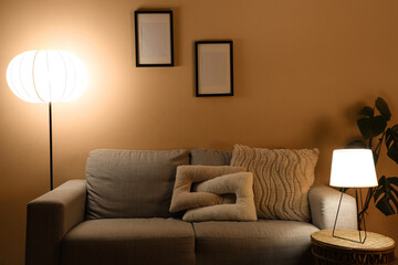 Interior of stylish living room with cozy grey sofa, coffee table and glowing lamps at evening
