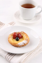 A delightful fruit Danish pastry, dusted with powdered sugar and topped with fresh strawberries and a blueberry