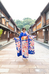 Fototapeta premium A teenage Japanese girl wearing a blue kimono stands in the view of a traditional town in a local Japanese city on a rainy summer day.