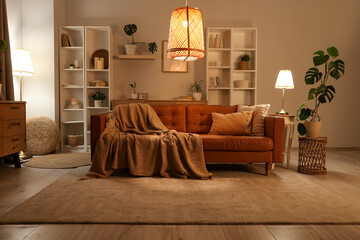 Interior of stylish living room with brown sofa, houseplants and glowing lamps at evening
