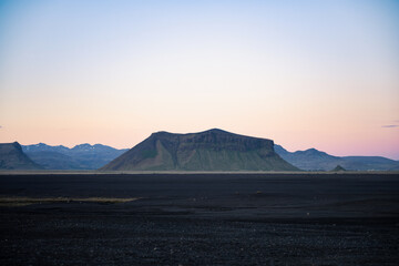 Flat-topped mountain in southern Iceland at dusk, rising from a vast black sand plain under a...