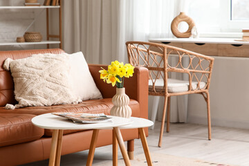 Vase of beautiful daffodil flowers and magazines on coffee table near sofa in living room