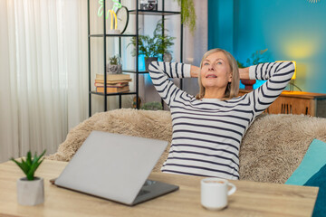 Mature woman happily closes laptop after completing important task. Caucasian grandmother sitting...