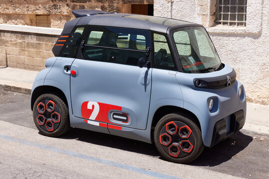 A light blue Citro&euml;n Ami microcar parked on street. This tiny electric quadricycle represents modern urban mobility in contrast to the ancient Mediterranean town setting. 26.06.2022, Monopoli, Italia