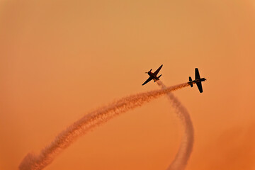 two planes synchronously flying during an aerial performance on the beatiful sunset orange sky