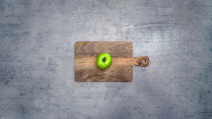 Perfect fresh green apple on a wooden cutting board with a gray background and blank space.