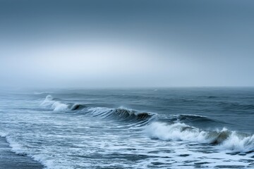 Fototapeta premium A serene ocean view captures the quiet majesty of waves rolling toward a misty horizon under a subtly colored sky, evoking calm and infinite tranquility.