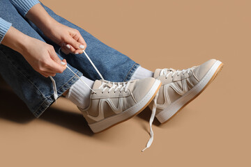Woman in stylish sneakers sitting on beige background, closeup