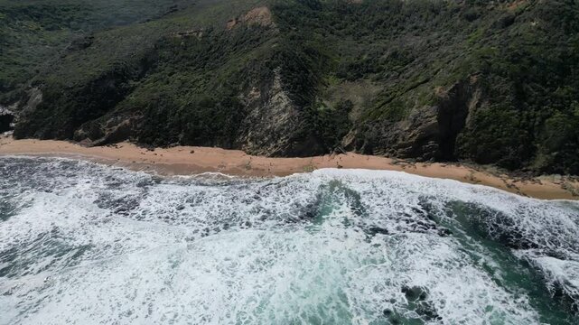 Drone view of Wreck Beach with crashing waves and green cliff on a sunny day with cloudy sky