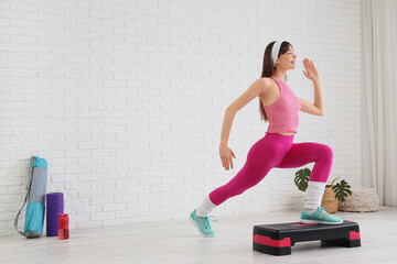 Sporty young woman exercising on aerobic stepper at home