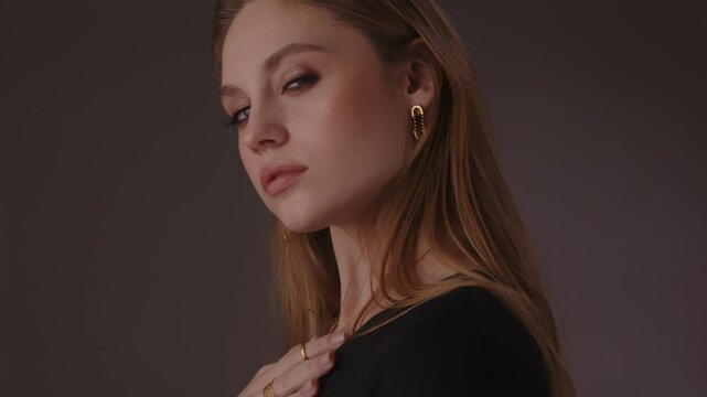 Beautiful girl with gold jewelry and loose hair in black clothes posing on a dark background. Beauty face and hair. Video 4k