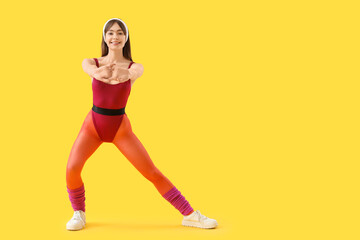 Sporty young woman doing aerobics on yellow background