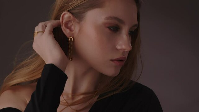 Beautiful girl with gold jewelry and loose hair in black clothes posing on a dark background. Beauty face and hair. Video 4k