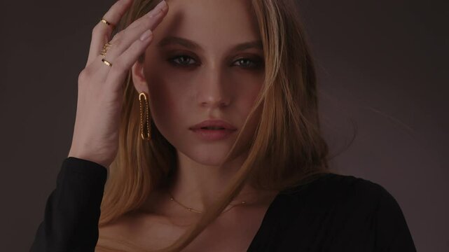 Beautiful girl with gold jewelry and loose hair in black clothes posing on a dark background. Beauty face and hair. Video 4k