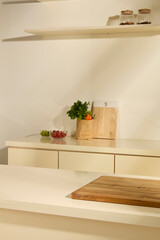 Vertical photo of the kitchen room. Vegetables in paper bags, next to glass bowls of tomatoes and green grapes. Empty wooden cutting board placed on white table in the middle of the kitchen