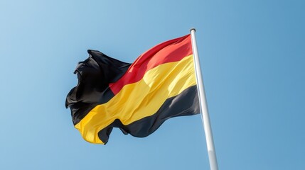 Black, yellow, and red Belgian banner fluttering against clear day sky, cultural expression