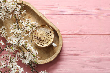 Wooden tray with cup of coffee and beautiful blooming tree branches on pink wooden background