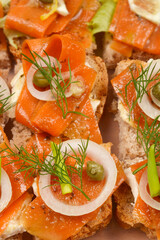 An assortment of open-faced sandwiches featuring carrot slices prepared as vegan salmon, arranged in a clear container